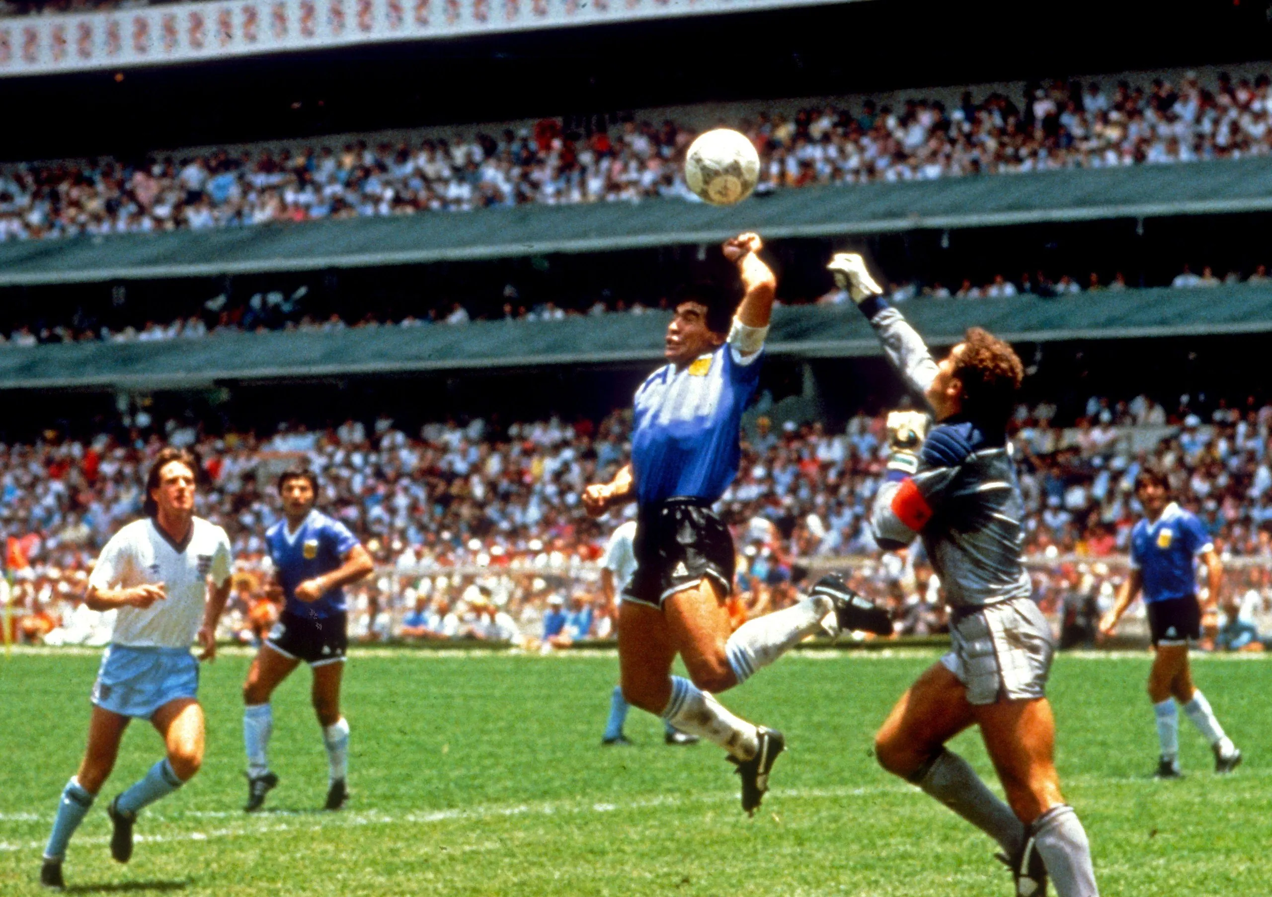 Diego Maradona leaping in the air with his hand just below a ball.